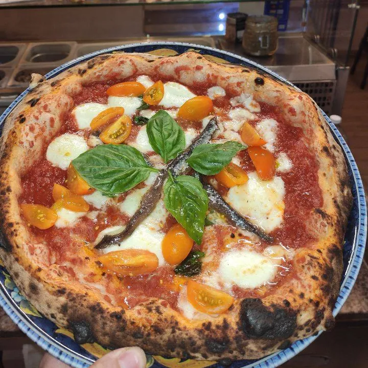 La pizza Eccellenza Campana vista dall'alto: pomodoro, bufala, pomodorini gialli, alici e foglie di basilico