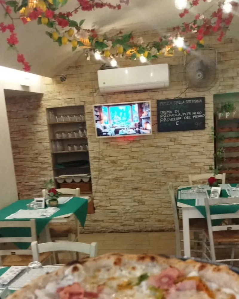 La sala della pizzeria: tovaglie verdi, sedie bianche impagliate, parete in pietra e bouganville con limoni al soffitto