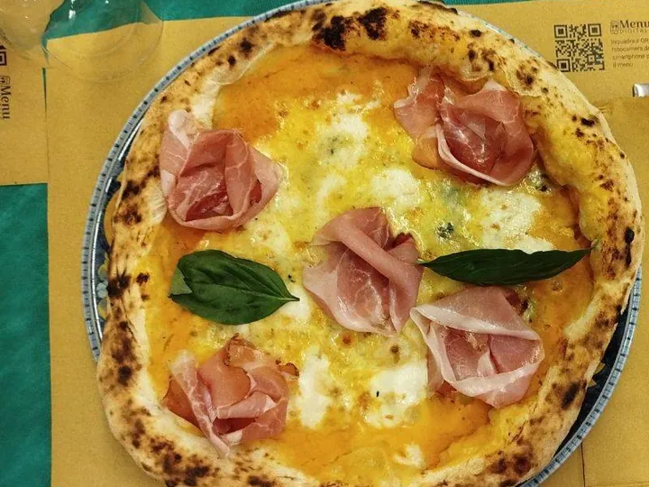 La pizza Sapori d'inverno, con crema di zucca e speck, sul tavolo apparecchiato